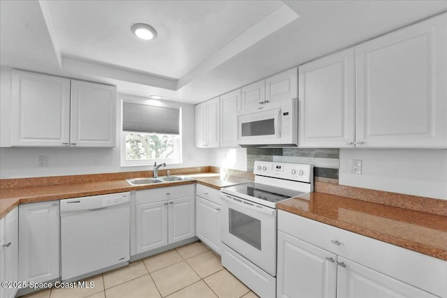 kitchen with light tile patterned flooring, white appliances, a sink, white cabinets, and a raised ceiling