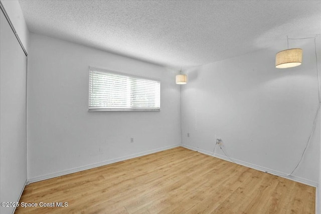 empty room with a textured ceiling, light wood finished floors, and baseboards