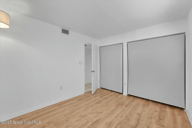 unfurnished bedroom featuring light wood finished floors, two closets, visible vents, a textured ceiling, and baseboards