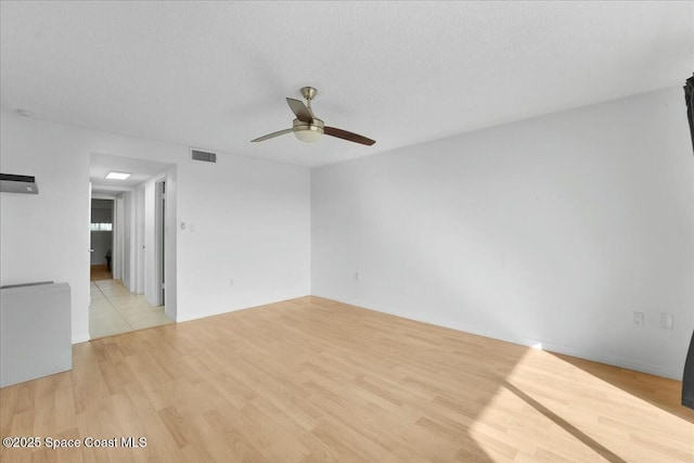 empty room featuring light wood-type flooring, ceiling fan, visible vents, and a textured ceiling