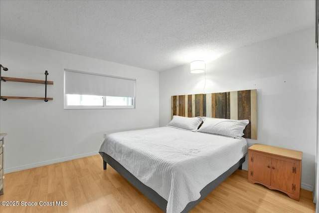 bedroom with a textured ceiling, light wood-type flooring, and baseboards