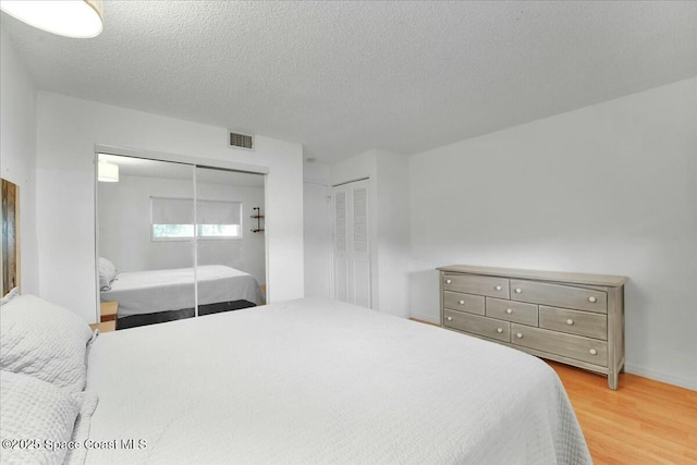 bedroom featuring light wood-type flooring, two closets, visible vents, and a textured ceiling