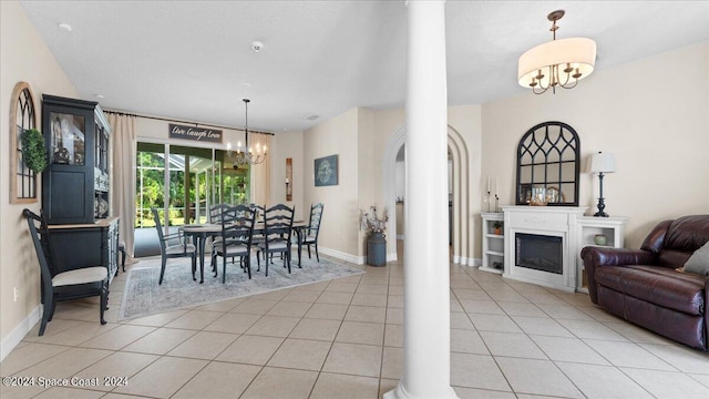 dining space featuring light tile patterned floors, a fireplace, baseboards, decorative columns, and an inviting chandelier