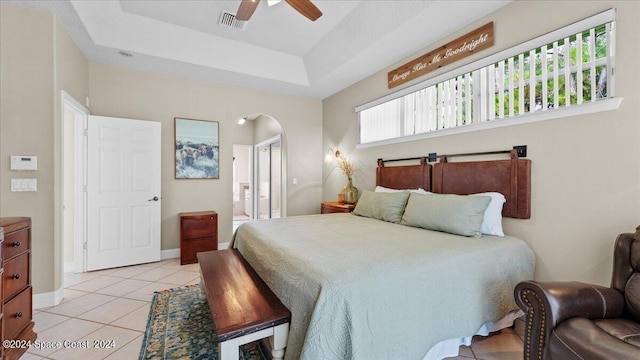 bedroom with light tile patterned floors, visible vents, arched walkways, a raised ceiling, and baseboards