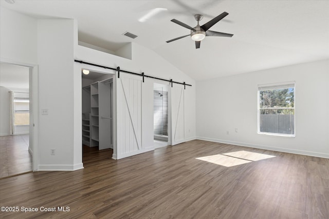 unfurnished bedroom with a barn door, vaulted ceiling, a closet, dark wood-style floors, and a walk in closet