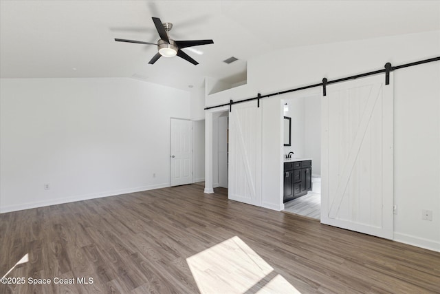 unfurnished bedroom with lofted ceiling, a barn door, and wood finished floors