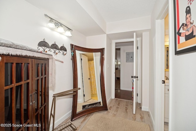 corridor with electric panel, light wood-style flooring, and baseboards