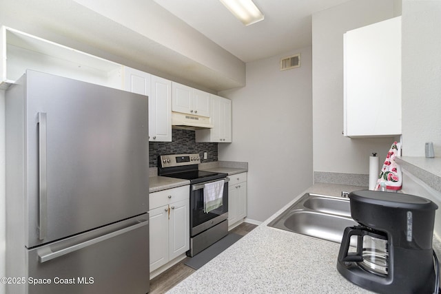 kitchen with appliances with stainless steel finishes, white cabinetry, under cabinet range hood, and decorative backsplash