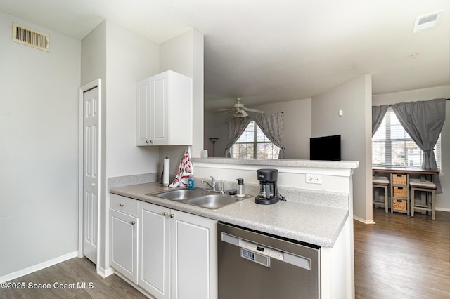 kitchen featuring visible vents, dishwasher, wood finished floors, a peninsula, and a sink