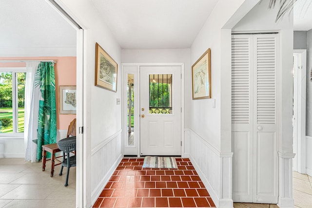 doorway to outside with wainscoting, a decorative wall, and tile patterned floors