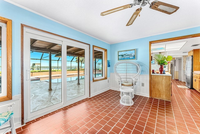 interior space featuring brick floor, a wainscoted wall, crown molding, a sunroom, and ceiling fan