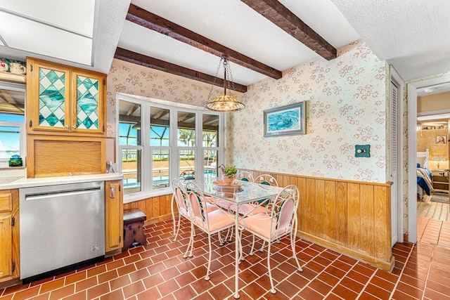 dining space featuring a textured ceiling, a wainscoted wall, brick patterned floor, beamed ceiling, and wallpapered walls