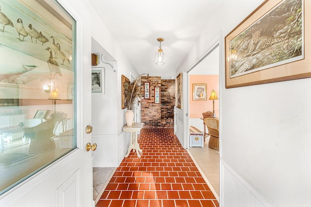 hall featuring a wainscoted wall, brick wall, and a decorative wall