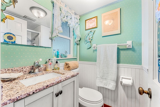 full bathroom featuring toilet, visible vents, vanity, wainscoting, and wallpapered walls