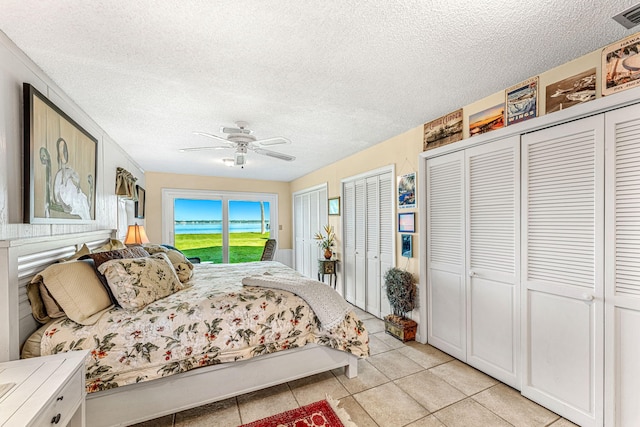 bedroom with light tile patterned floors, ceiling fan, a textured ceiling, access to exterior, and two closets