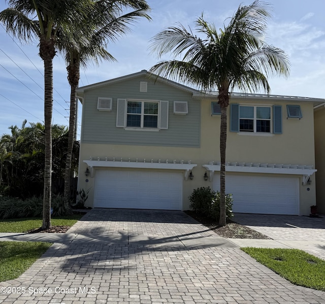 view of front of home with decorative driveway, a wall mounted air conditioner, an attached garage, and stucco siding