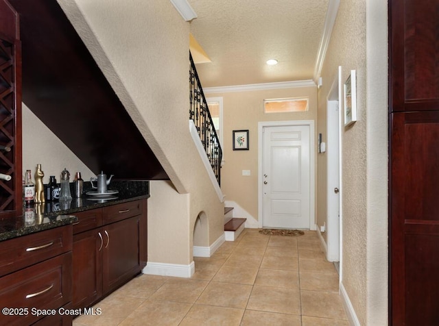 entryway with light tile patterned floors, baseboards, ornamental molding, stairs, and a textured ceiling