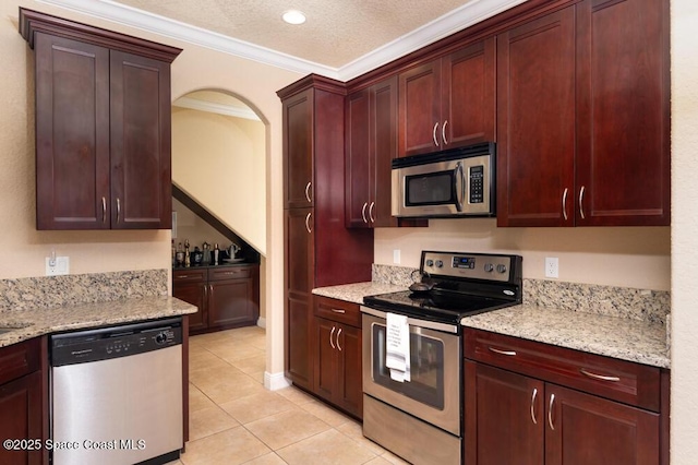 kitchen with light tile patterned floors, arched walkways, appliances with stainless steel finishes, light stone counters, and crown molding