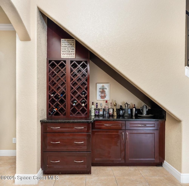 wine area with a dry bar, light tile patterned floors, lofted ceiling, a textured wall, and baseboards