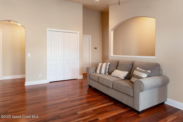 living room with dark wood-style floors, visible vents, baseboards, and arched walkways