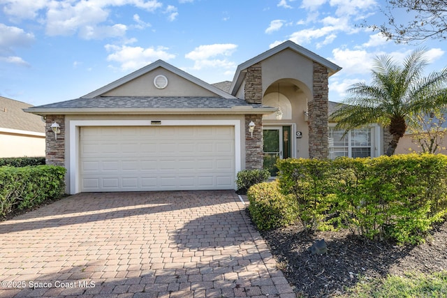 traditional home with an attached garage, a shingled roof, stone siding, decorative driveway, and stucco siding