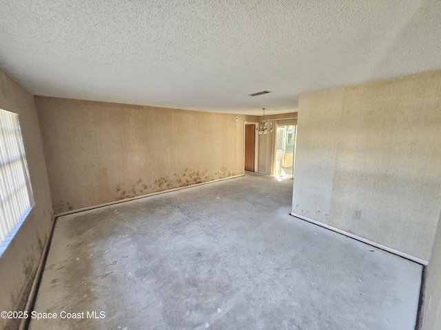 spare room featuring a textured ceiling, unfinished concrete flooring, visible vents, and an inviting chandelier