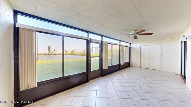 unfurnished sunroom with a ceiling fan, a water view, and plenty of natural light