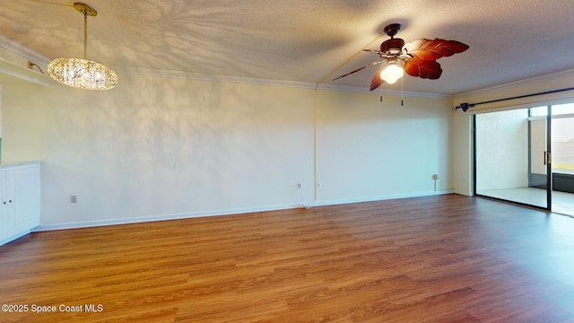 spare room featuring ceiling fan with notable chandelier, baseboards, wood finished floors, and crown molding