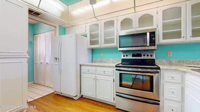kitchen with light wood-style flooring, stainless steel appliances, visible vents, light countertops, and glass insert cabinets
