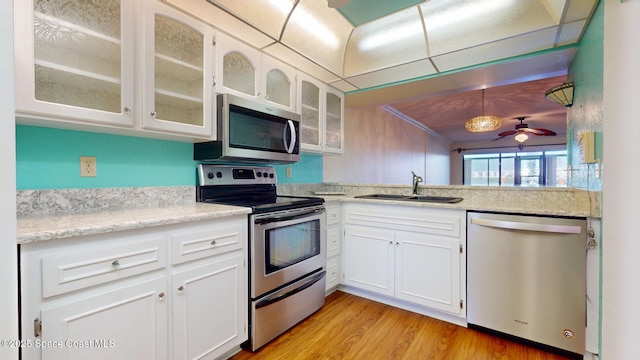 kitchen with a sink, white cabinets, appliances with stainless steel finishes, light wood-type flooring, and glass insert cabinets