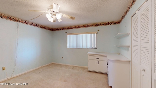 interior space featuring a ceiling fan, light carpet, a textured ceiling, and baseboards
