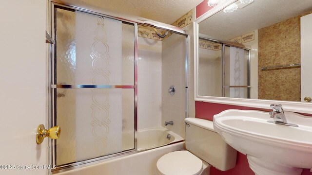 bathroom featuring combined bath / shower with glass door, a sink, a textured ceiling, and toilet