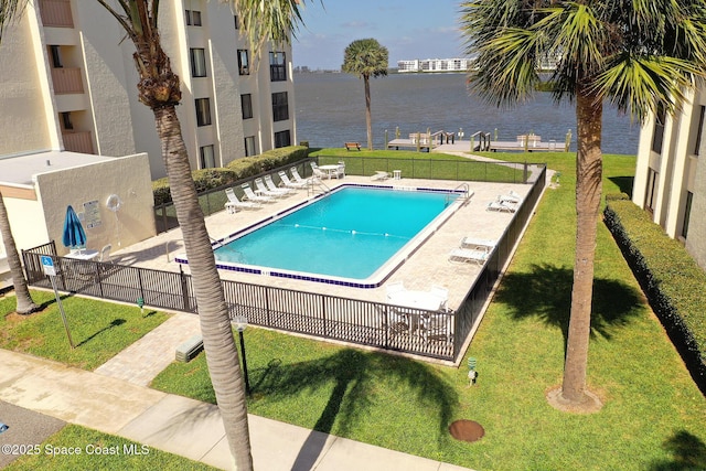 pool with a water view, a patio area, fence, and a yard