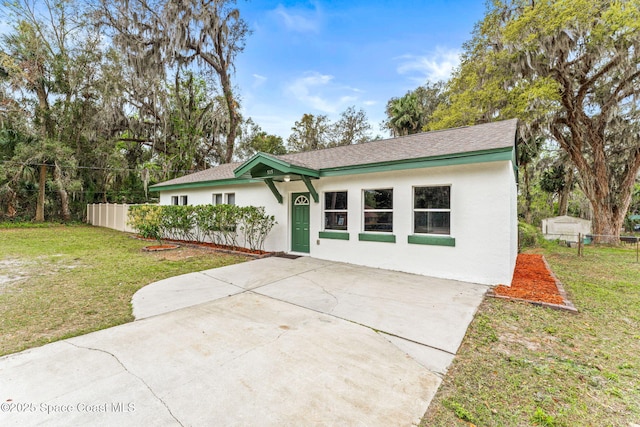 view of front facade featuring a shingled roof, fence, a front lawn, and stucco siding