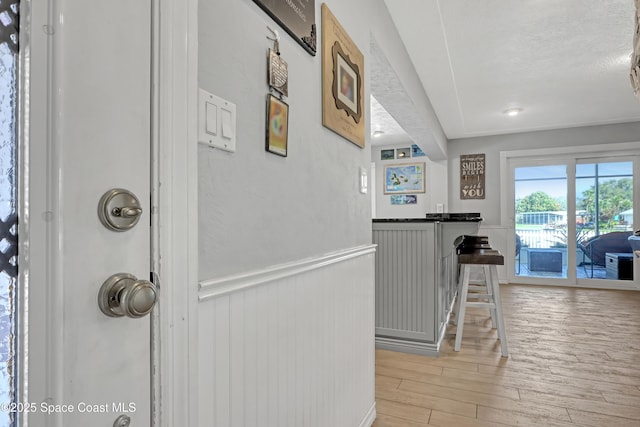 hallway with a textured ceiling, light wood-style flooring, and wainscoting