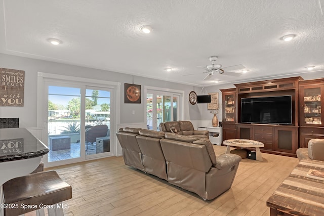 living room featuring ceiling fan, light wood finished floors, and a textured ceiling