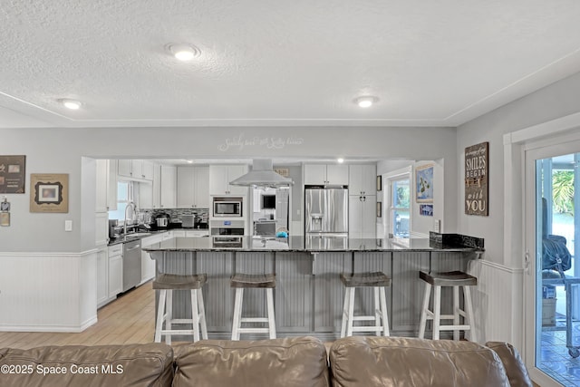 kitchen featuring white cabinetry, ventilation hood, a peninsula, appliances with stainless steel finishes, and a breakfast bar area