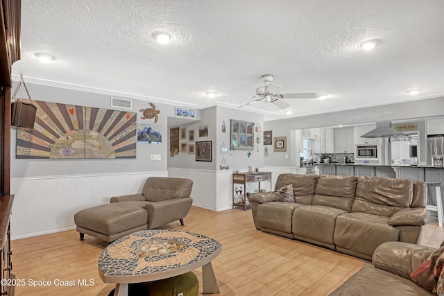 living room featuring visible vents, a textured ceiling, a wainscoted wall, and light wood-style flooring