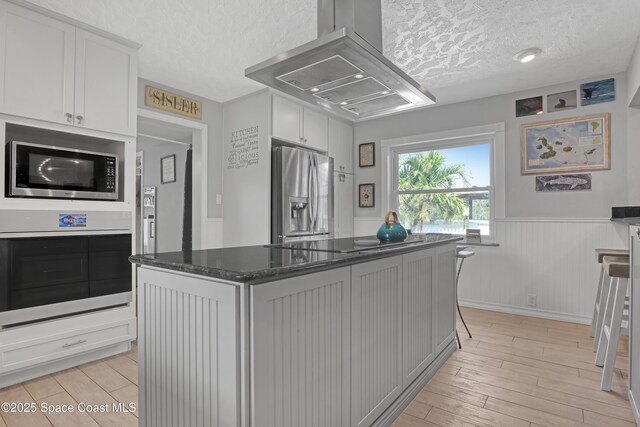 kitchen with a textured ceiling, stainless steel appliances, light wood-style floors, and island range hood