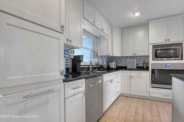 kitchen featuring decorative backsplash, light wood-style flooring, stainless steel appliances, a textured ceiling, and a sink