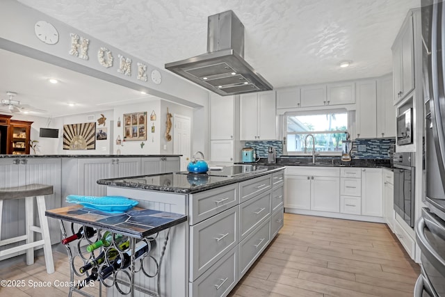 kitchen with decorative backsplash, gray cabinets, light wood-style flooring, island range hood, and a sink