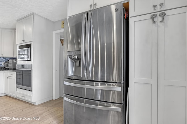 kitchen featuring light wood finished floors, decorative backsplash, white cabinets, appliances with stainless steel finishes, and a textured ceiling