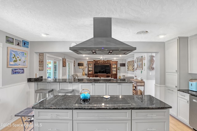 kitchen with light wood-type flooring, visible vents, a wainscoted wall, island exhaust hood, and black electric cooktop