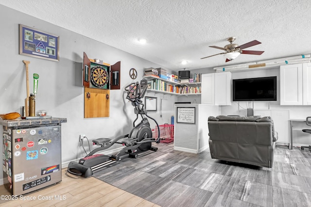 workout area with baseboards, a textured ceiling, a ceiling fan, and wood finish floors