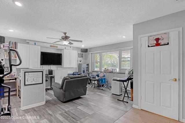 living room with light wood-type flooring, baseboards, a textured ceiling, and a ceiling fan