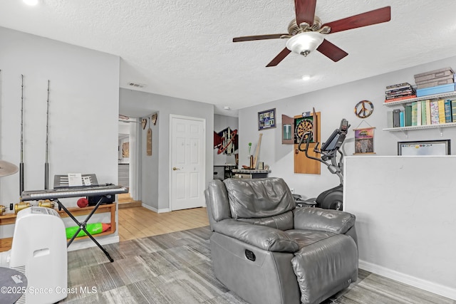 living area featuring wood finished floors, baseboards, visible vents, ceiling fan, and a textured ceiling