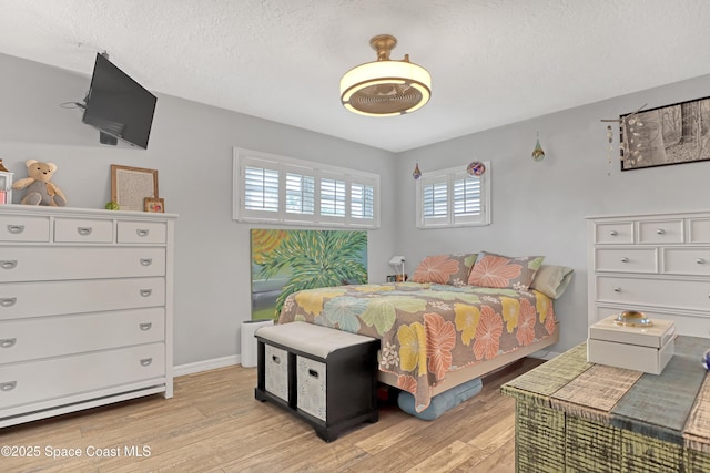 bedroom with baseboards, a textured ceiling, and light wood-style floors