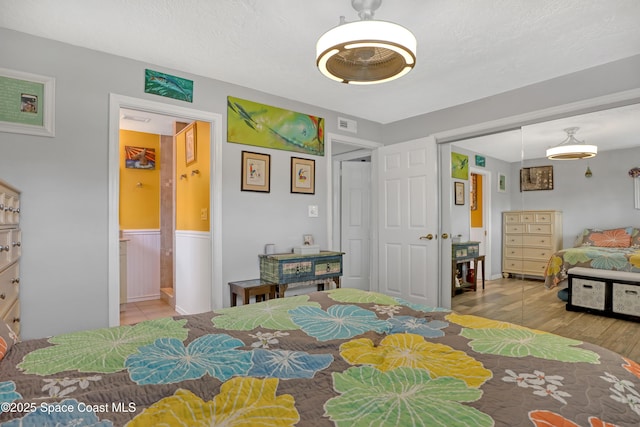 bedroom featuring visible vents, a textured ceiling, wood finished floors, a closet, and wainscoting