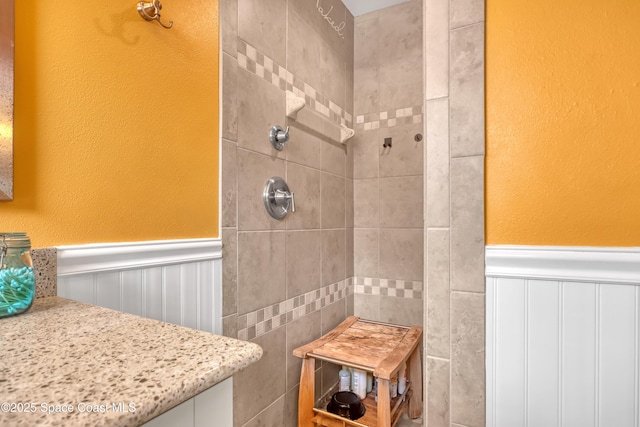 bathroom featuring wainscoting, tiled shower, and a textured wall