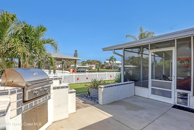 view of patio / terrace featuring a sunroom, a grill, exterior kitchen, and fence